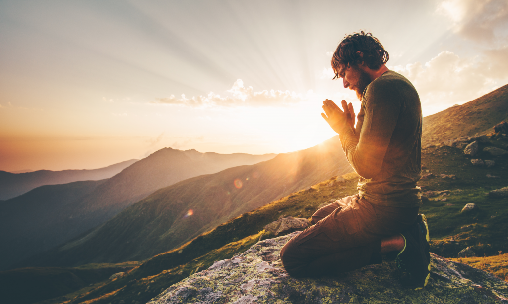 A person kneeling in reflection on a mountain at sunrise